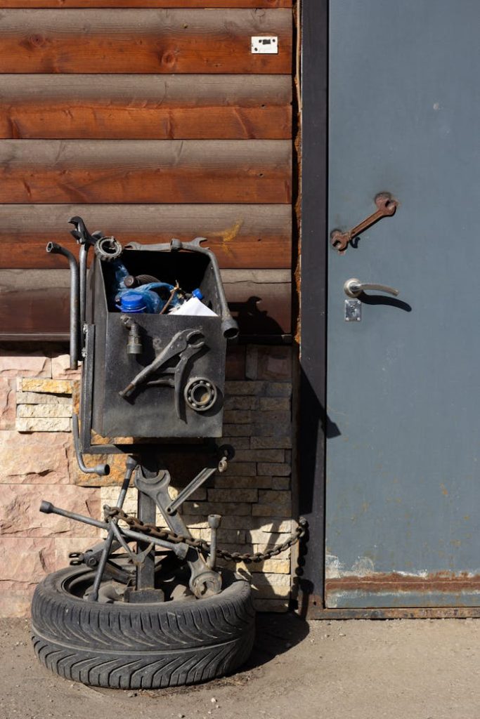 A collection of tools in a workshop setting next to a rustic metal door and a tire.
